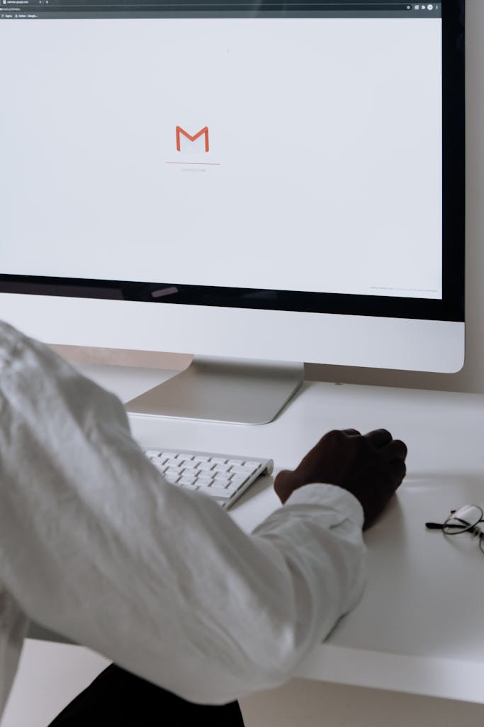 A local marketing professional in an office setting checking emails on a desktop computer with a clean workspace.