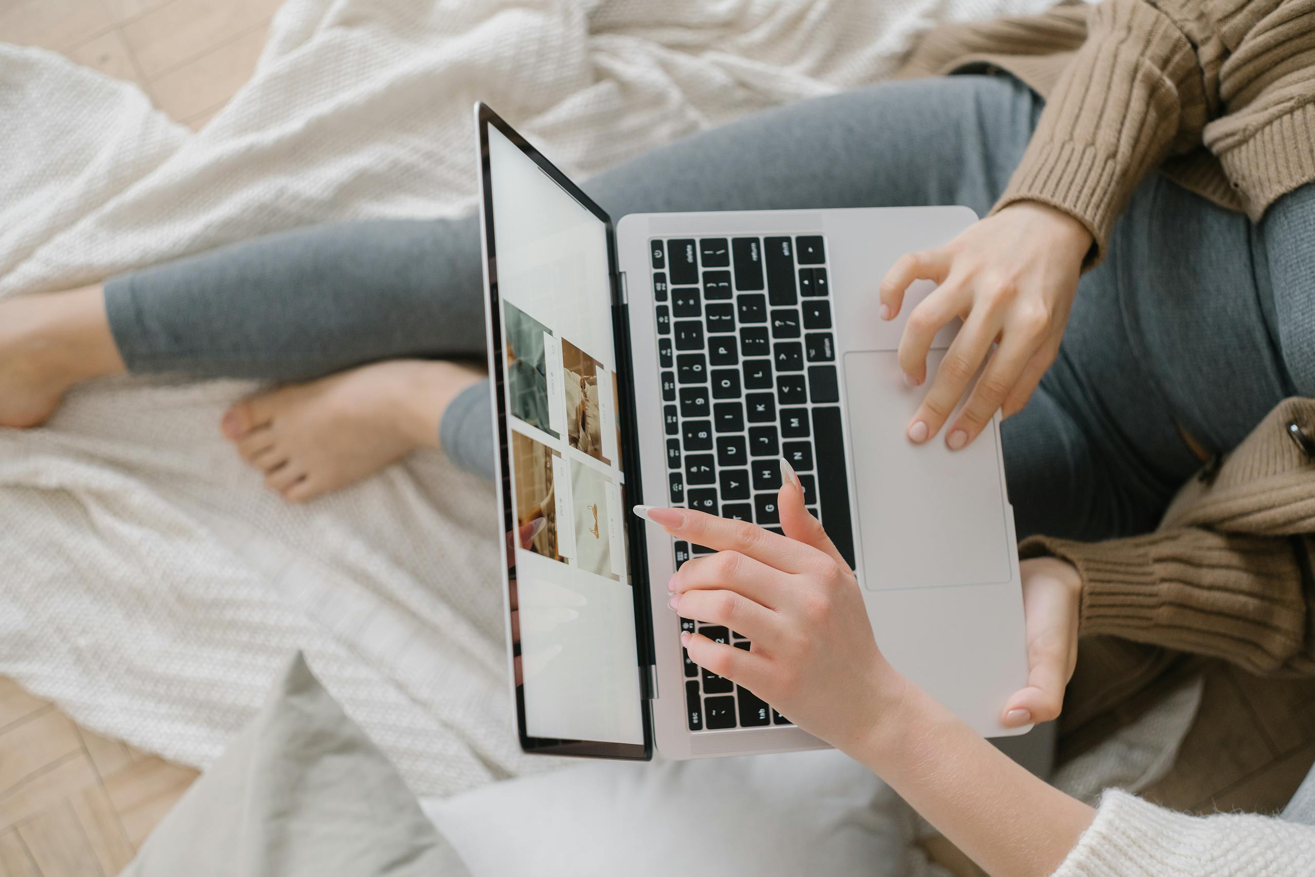 Pay Per Click 1 A woman leans on a cozy bed using a laptop, browsing images. Indoor setting.