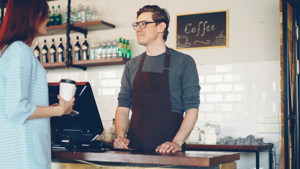 Search Engine Optimization 2 Barista in apron conversing with a customer at a cozy coffee shop counter.