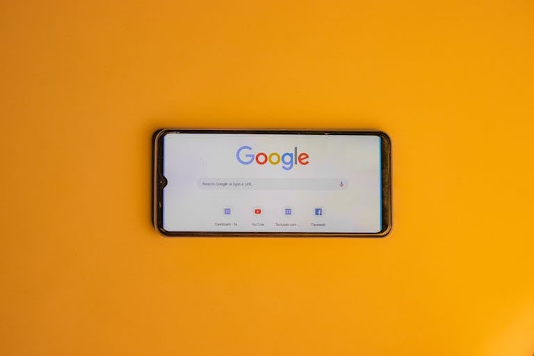 Smartphone displaying Google search page on a vibrant yellow background.