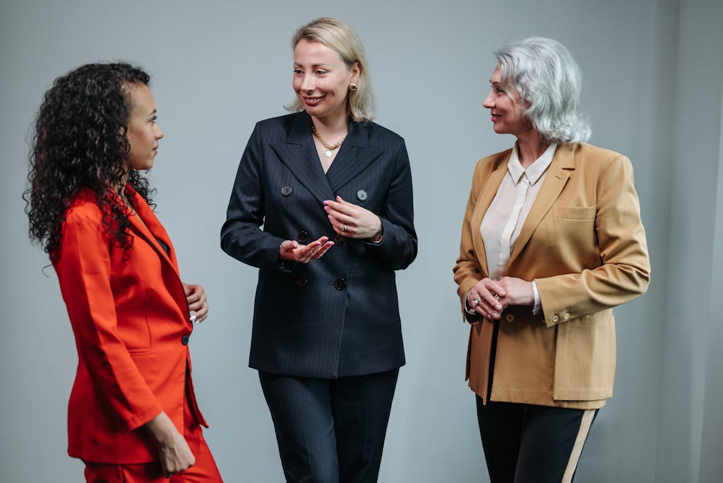 Three women in business attire having a conversation indoors, showcasing diversity and teamwork.