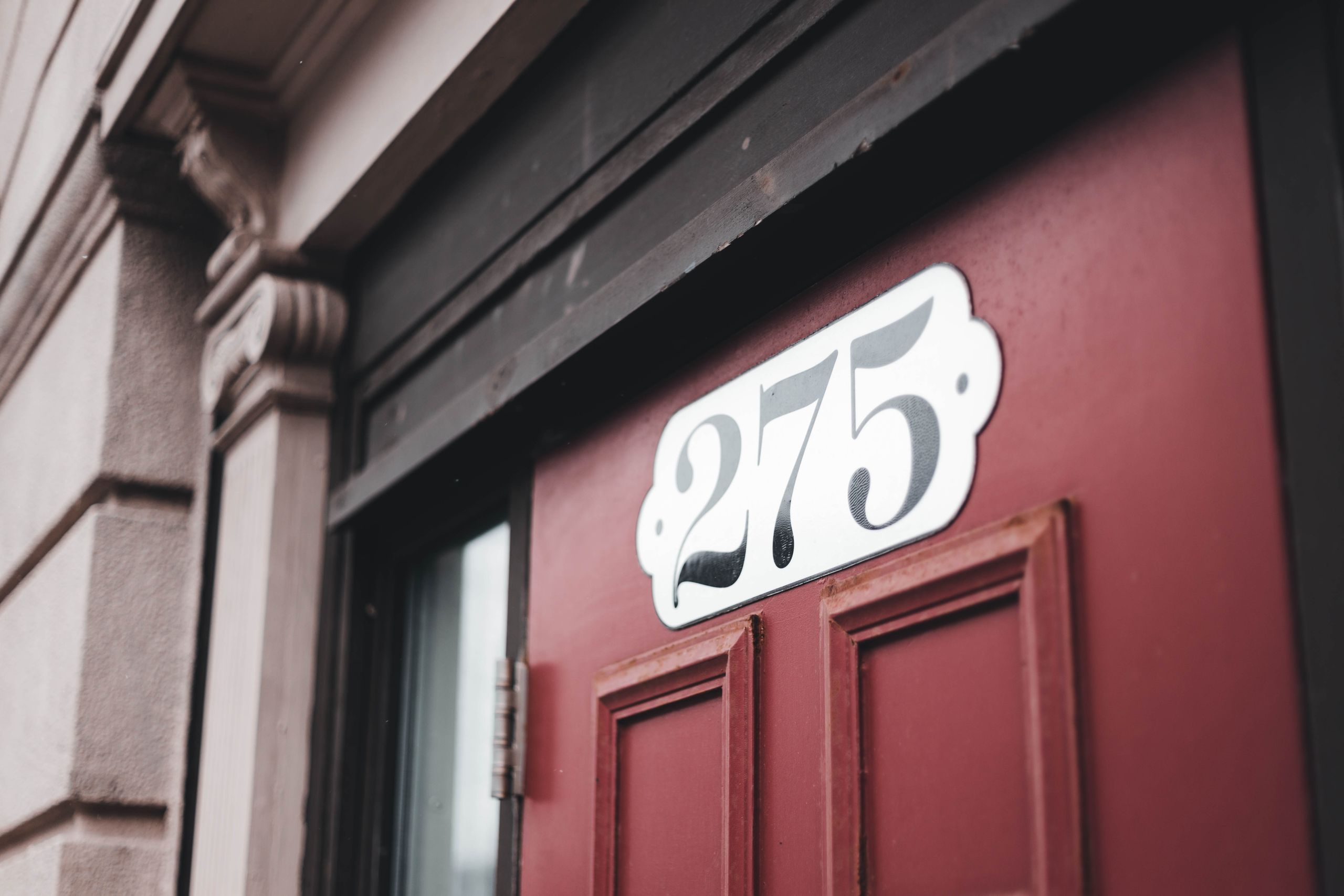 Close-up of a red door featuring a decorative number 275 sign, urban architecture.